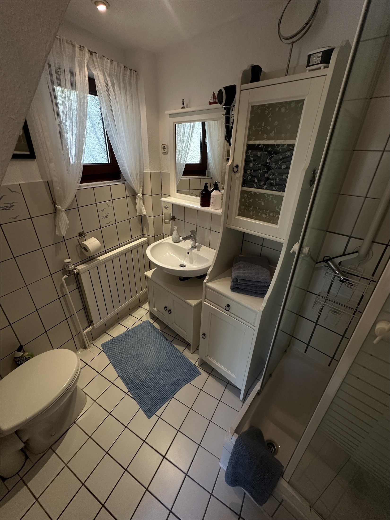 Duschbad mit Waschbecken, Dusche, WC und hellen Fliesen